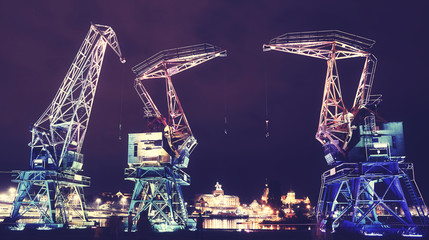 Illuminated old port cranes on a boulevard in Szczecin City at night, color toning applied, Poland. - obrazy, fototapety, plakaty