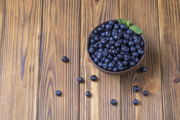 Fresh blueberry in ceramic bowl on wooden table.