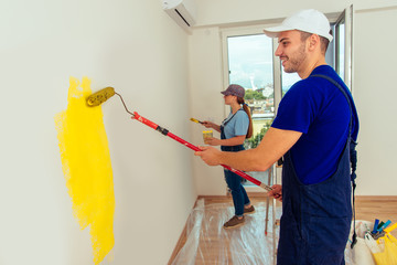 Smiling couple painting wall at home in yellow color