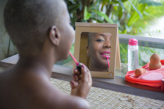 beautiful black afro American woman applying face makeup using brush on her lips looking herself in the mirror at home garden in beauty concept