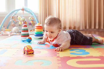 Portrait of cute adorable blond Caucasian smiling child boy with blue eyes crawling on floor in kids children room. Little baby playing with toys on playmat at home. Early education development - obrazy, fototapety, plakaty
