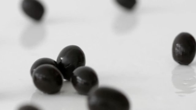 Black olives rolling on a mirror-white surface in slow motion