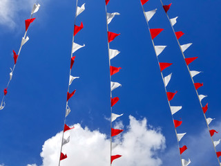 Garland of red and white triangle flags on blue sky background.