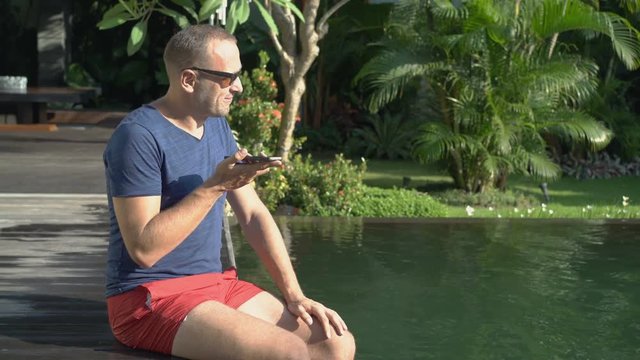 Young, handsome man talking on cellphone by the swimming pool
