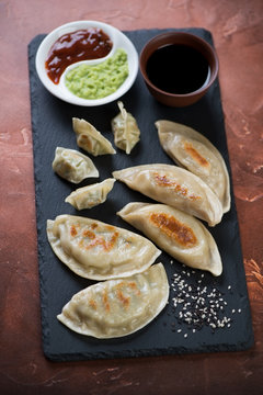Stone slate with different types of fried korean dumplings and dipping sauces, studio shot