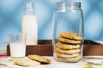 Composition with a cookie pile and milk bottle in a table. Morning sun in a blue background with texture.