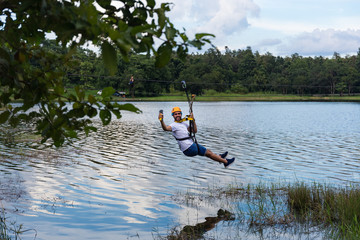 Young man goes through a lagoon on zip line in Chiang Mai in Thailand © LAMBERTOJESUS