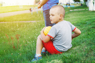 A boy is sitting on the grass with a yellow ball in his hands