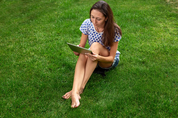young girl blogger. the girl is working on the tablet. the girl is sitting on the green lawn