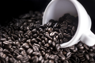 Black coffee beans in white cup on dark surface. Close up.