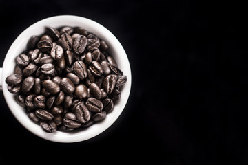 Black coffee beans in white cup on dark surface. Close up.