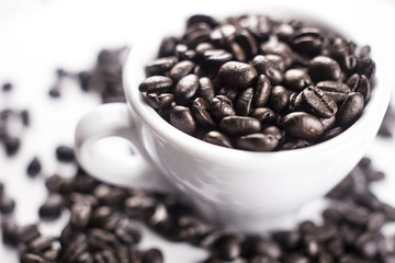 Brown coffee beans in white cup isolated on white background.