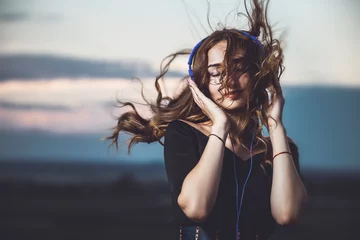 Fotobehang portrait of a beautiful girl in headphones listening to music on nature © fantom_rd