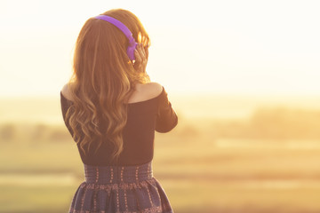 girl in headphones listening to music on nature at sunset in the field