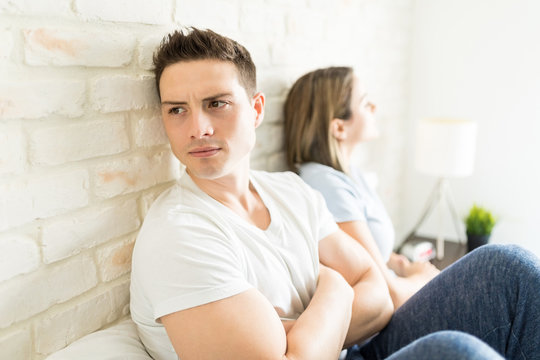 Angry Man Looking Away While Sitting By Girlfriend On Bed