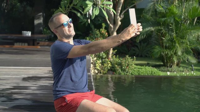 Man taking photo with tablet computer by luxury swimming pool
