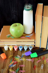 Books, stationery, green apple and milk on a wooden table