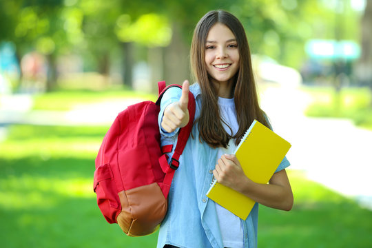 Cute girl with backpack and notebook in the park
