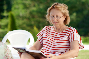 Aged Caucasian woman reading book at home patio.