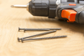 Wireless screwdriver and self-tapping screws on a wooden background, the theme of repair work, close-up