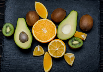 Fruit platter on a black  slate board: kiwi, orange, avocado