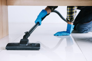 Housekeeping and housework cleaning concept, Happy young man in blue rubber gloves using a vacuum cleaner on floor at home