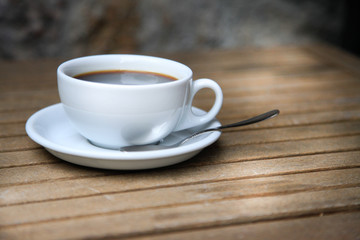 White cup with brown coffee on a wooden table.