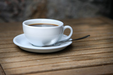 White cup with brown coffee on a wooden table.