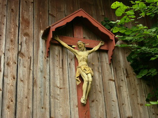 Kunstvoll geschnitztes Kruzifix mit dem leidenden Jesus am Kreuz an der Holzfassade einer alten...