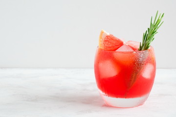 Refreshing cocktail of grapefruit with ice and rosemary on soft light white wood background....