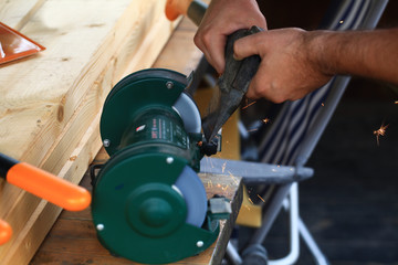 man sharpens an ax on a stone grinding wheel, and flying sparks.