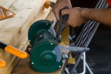 man sharpens an ax on a stone grinding wheel, and flying sparks.