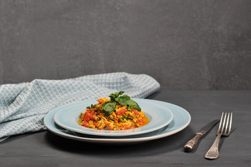 Scrambled eggs in Turkish menemen with tomatoes, green pepper and fresh herbs. Next to the plate are cutlery and a cloth slick. Gray background. Close-up.