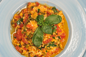 Scrambled eggs in Turkish menemen with tomatoes, green pepper and fresh herbs. The dish is decorated with basil leaves. View from above. Close-up. Macro photography.