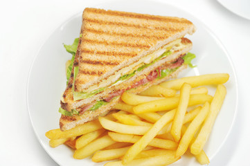 Fried french fries on a white plate. Next to the potato is a half-club sandwich with chicken meat and bacon. White background. Close-up. Macro photography. View from above.