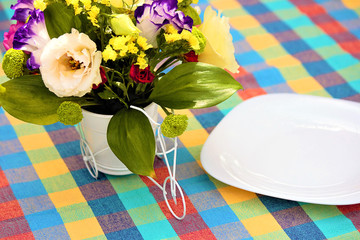 On the table are empty plates and a bouquet of flowers in a decorative vase. Colorful tablecloth on the table. Rustic background. The concept of a holiday. Selective focus, copy space.