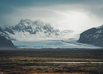 Road leading towards huge glacier and mountains in Iceland Vatnajokull glacier aerial drone image with street highway and clouds and blue sky. Dramatic winter scene of Vatnajokull National Park