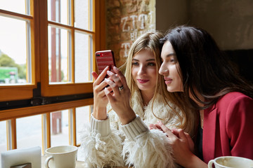 Two happy pretty young girls with smartphone drinking coffee in cafe .Technology, lifestyle and people concept -