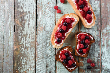 Healthy snack. Berry jam with fresh raspberries and currants on toasts on shabby blue background copyspace