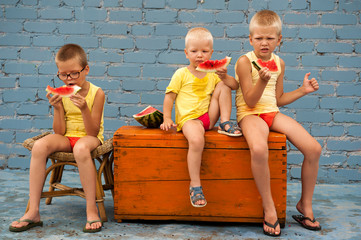 Funny village children eat watermelon sitting on old chest in courtyard of village house. Boys...