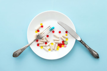 Many different weight loss pills and supplements as food on round white plate with fork and knife....