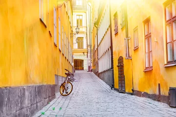 Papier Peint photo Stockholm The narrow cobblestone street with a bicycle and yellow medieval houses of Gamla Stan historic old center of Stockholm at summer sunny day.