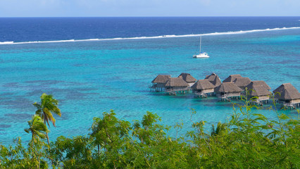 Small emerald ocean waves splash and approach wooden bungalows of luxury resort.