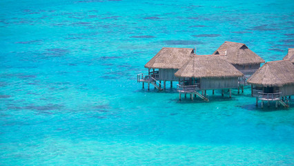 Tranquil turquoise ocean water surrounds the wooden bungalows on a sunny day.