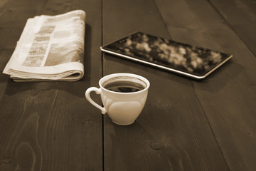 A cap of coffee newspaper and tablet - sepia color