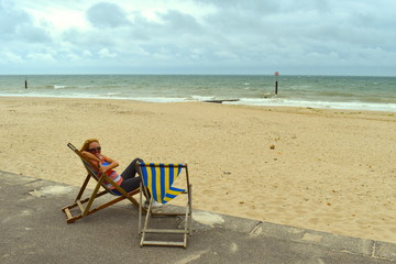 Fototapeta na wymiar Blond girl sitting on a deck chair on the beach, Bournemouth, England