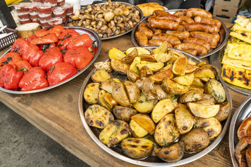 fried potatoes sliced in large slices laid out on a large metal plate, with fried sausage and baked vegetables and ketchup in plastic containers on a fast food table