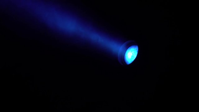 One searchlight turns in multicolored beams on a black background