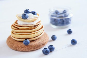 Delicious homemade pancakes with yogurt and fresh blueberries on white wooden background.