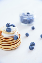Delicious homemade pancakes with yogurt and fresh blueberries on white wooden background.